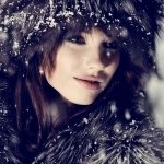 Profile photo of a woman with dark hair and fur clothing, snowflakes falling gently around her face, creating a serene winter atmosphere.