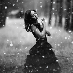 Black-and-white forum avatar/pfp of a woman in a dark dress smiling amid falling snow, with a blurred winter forest background.