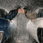 Forum avatar of a woman kissing a partner beneath a heavy downpour between two cars, a romantic image conveying love.