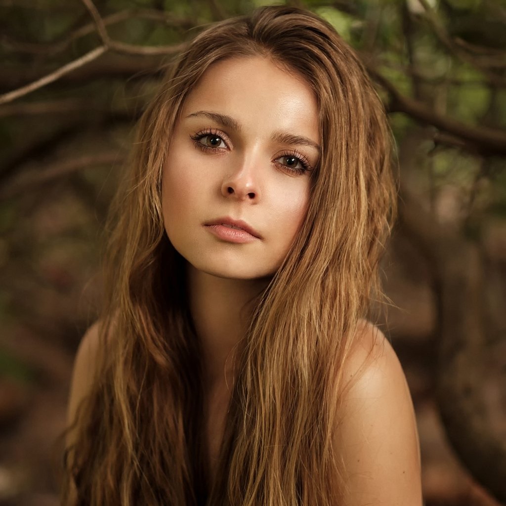 Profile avatar of a brunette model with long hair and brown eyes, neutral expression against a soft outdoor background.