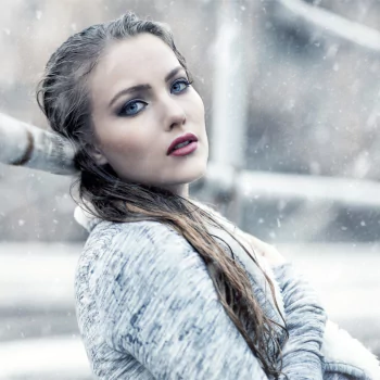 Forum avatar: portrait of a brunette woman model with blue eyes and lipstick, glancing over her shoulder in a snowy outdoor setting.