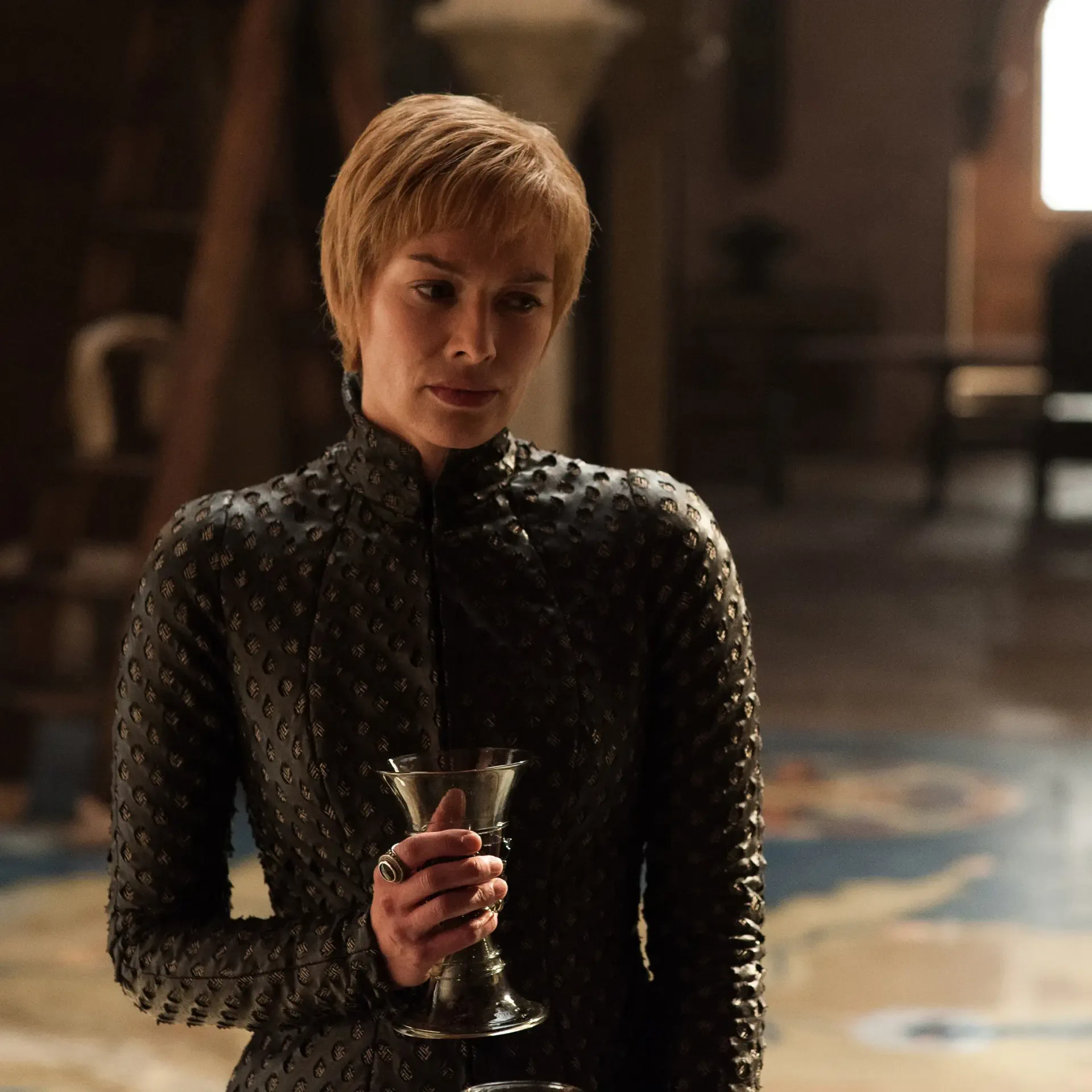 Cersei Lannister, portrayed by Lena Headey, stands elegantly in a dark, spiked outfit, holding a glass, showcasing her strong presence from the TV show Game of Thrones.