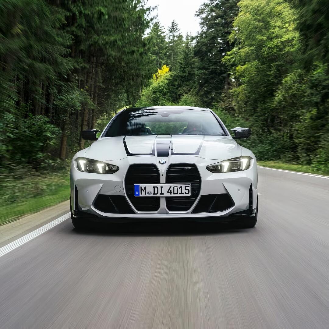 Front view of a white BMW M4 driving on a forest-lined road, used as a forum avatar or profile photo.