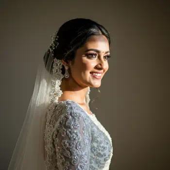A smiling bride in an ornate dress and veil, showcasing delicate details and elegant jewelry, captured in a soft, glowing light for a forum avatar or profile photo.