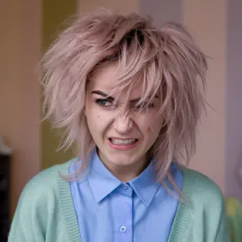 A young person with messy pink hair displays a mad expression, wearing a blue shirt and green cardigan. This image serves as a forum avatar, capturing a bold emotional tone.