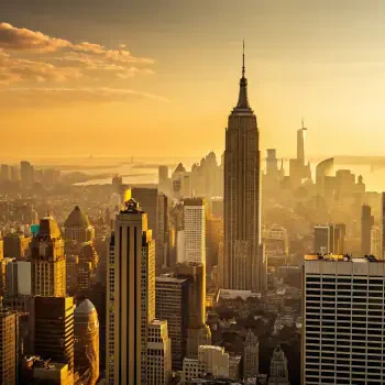 A breathtaking view of Manhattan at sunset, showcasing the iconic Empire State Building surrounded by skyscrapers, creating a warm golden ambiance in the skyline.