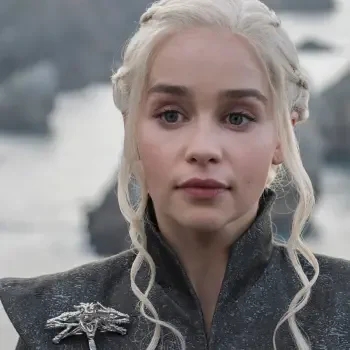 A close-up of Daenerys Targaryen, portrayed by Emilia Clarke, from Game of Thrones. She has platinum blonde hair, wearing a dark outfit, with a serious expression against a scenic backdrop.