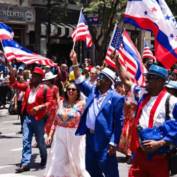 Crowd celebrating Juneteenth in colorful attire, waving American and Pan-African flags during a lively street parade.