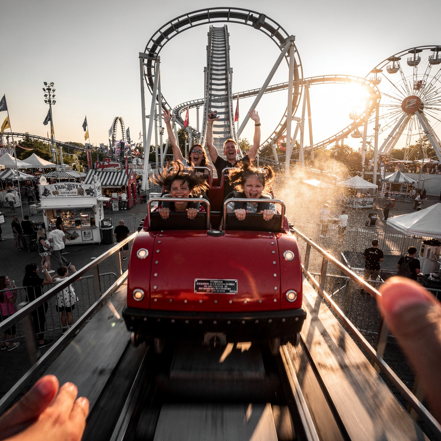 Forum avatar/profile photo of a red roller coaster car hurtling toward the viewer, riders cheering as carnival lights and a Ferris wheel glow at sunset.