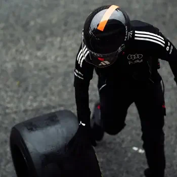Forum avatar/pfp of an Audi F1 driver in a black race suit and helmet, pushing a tire in a top-down view.