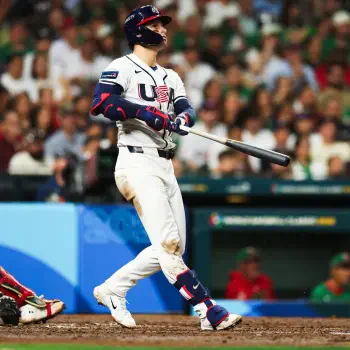Forum avatar of a baseball player in a USA Baseball uniform swinging a bat at the plate, dirt-streaked pants and a packed crowd behind, used as a profile photo.