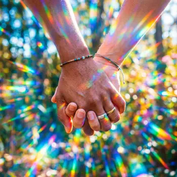 Forum avatar/pfp of two hands holding, rings and bracelets visible, rainbow prism light streaks radiate across a colorful bokeh background.