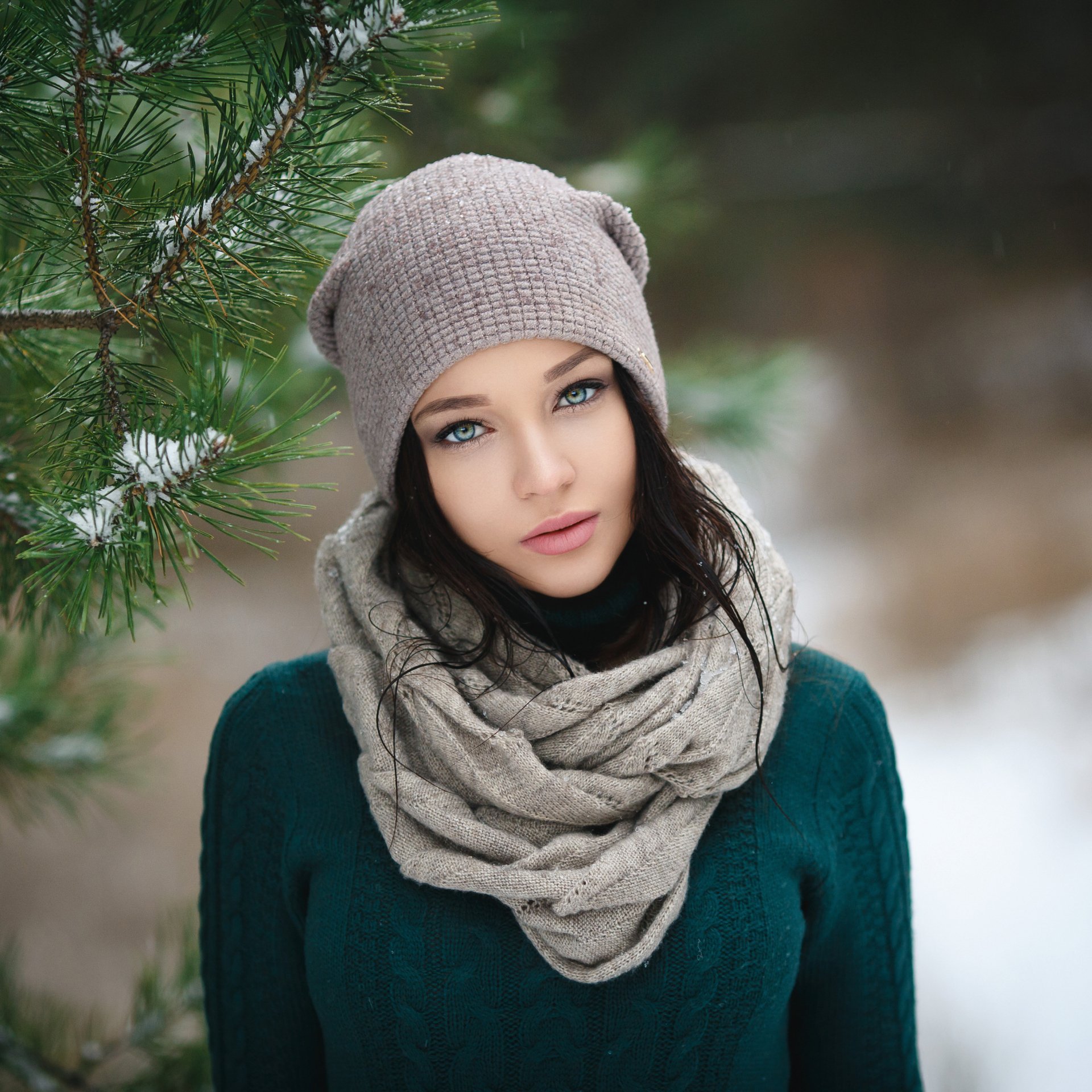 Forum avatar of a young woman model wearing a knit hat and chunky scarf, gazing against a snowy pine background.