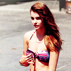 Avatar-style profile photo of a young female celebrity in a patterned bikini top, hair swept to one side, looking off-camera with a relaxed expression.