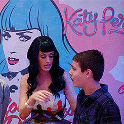 Music-themed forum avatar: a dark-haired woman talking with a young fan in front of a colorful poster featuring a stylized blue‑haired performer.