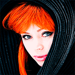 Forum avatar of a fantasy redheaded woman in a dark hood, vivid orange hair framing her face, pale skin and one eye caught in a playful blink toward the viewer.